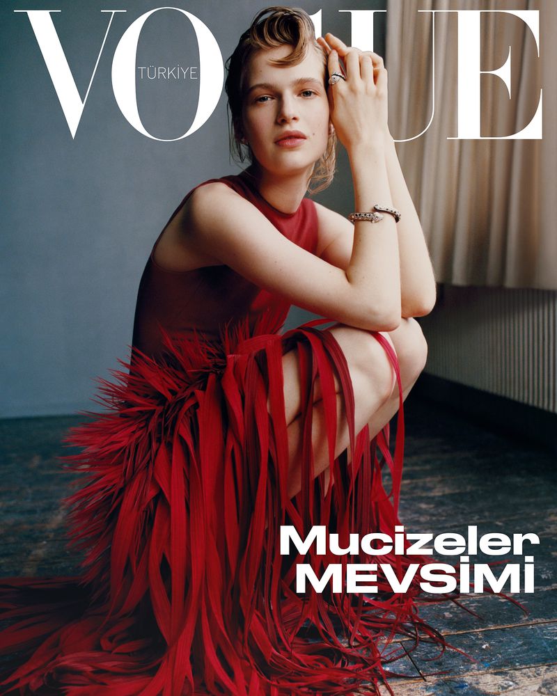 Vogue Turkiye magazine cover featuring a young woman with light skin and red dress kneeling, hands near her face in a studio setting.