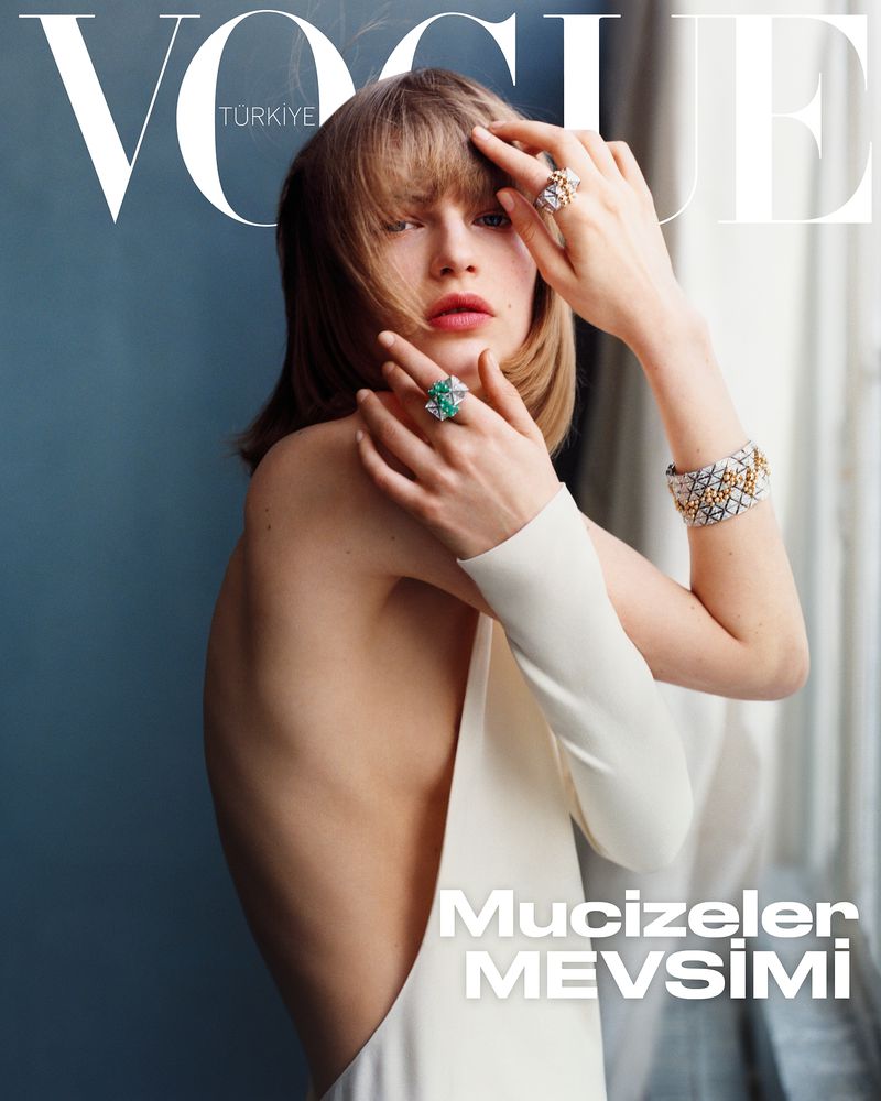 Model wearing white dress and statement rings posing against blue wall for Vogue Turkey December 2024 cover