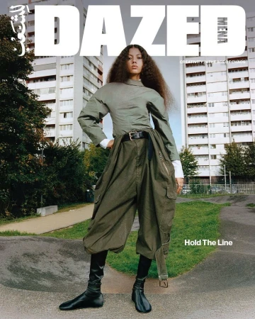 Editorial fashion shot of a young adult woman with curly hair wearing an olive green top, baggy pants, and black boots in an urban setting.