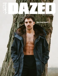 Saint Levant posing shirtless under a dark fur-lined hooded parka against a tree trunk for Dazed MENA cover