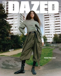 Model standing outdoors wearing an olive green utility outfit and black boots against residential buildings