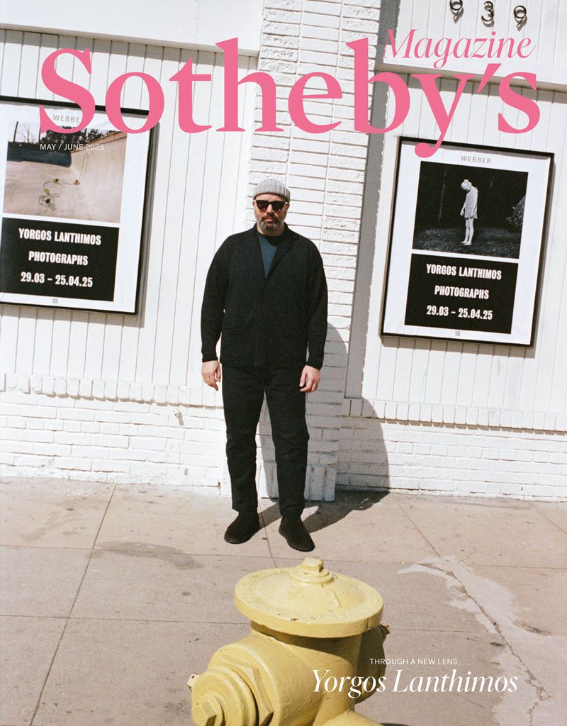Magazine cover featuring Yorgos Lanthimos standing on a sidewalk next to art exhibition posters and a yellow fire hydrant in daylight.