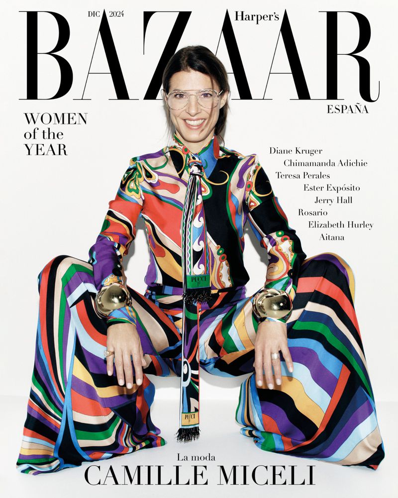 Camille Miceli cover of Harper's Bazaar España. Woman in colorful patterned outfit, large gold bracelets, glasses, seated pose on white.