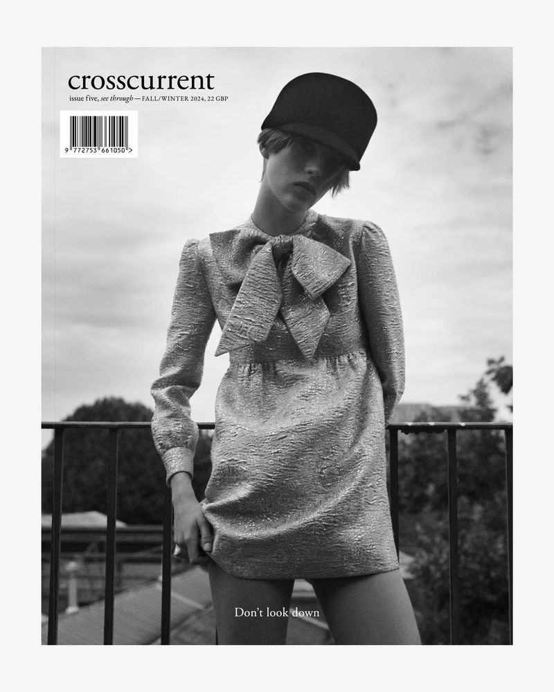 Black and white fashion magazine cover featuring a woman in a shimmering dress, black cap, and a cloudy sky backdrop.