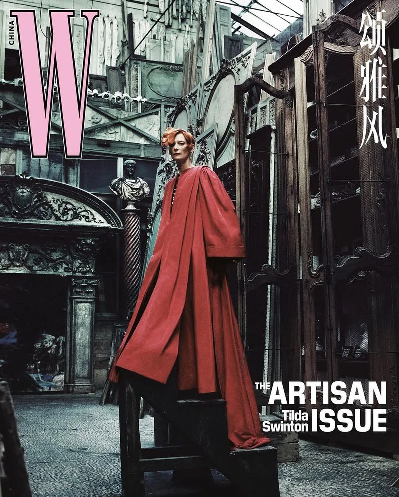 Magazine cover featuring Tilda Swinton in a red coat, standing on a ladder against a backdrop of antique architectural salvage.