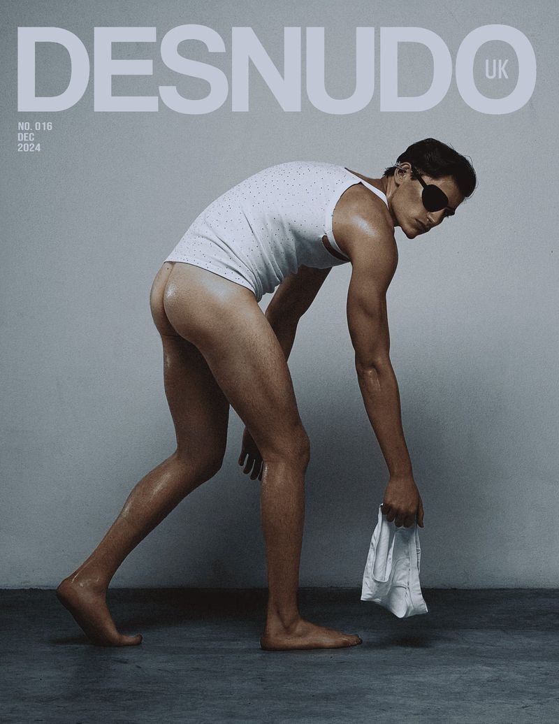 Man in tank top and sunglasses holding a cloth, posing for a magazine cover; 'Desnudo UK' text visible, neutral studio background and muted colors.