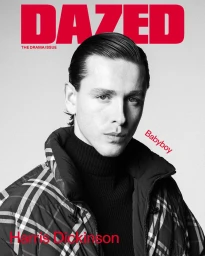 Portrait of Harris Dickinson wearing a black turtleneck and plaid puffer jacket against a white background for Dazed Magazine