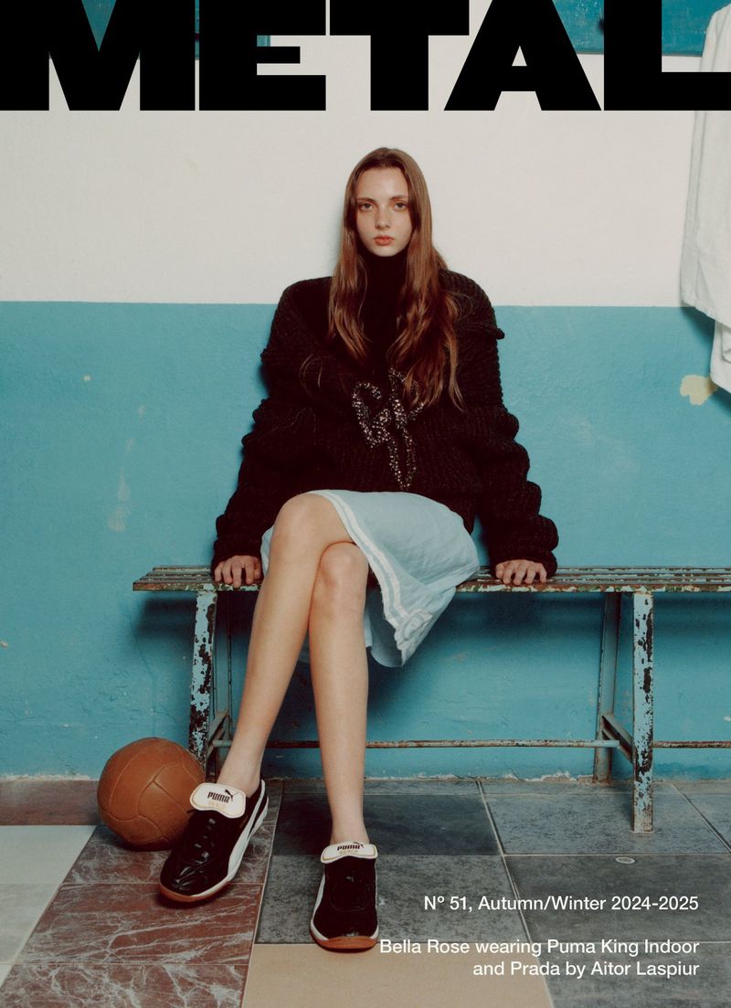 Fashion editorial image: a model sits on a bench wearing a dark sweater, light blue skirt, and black sneakers with a basketball nearby.
