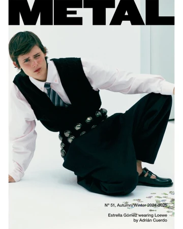 Magazine cover featuring a young person with short brown hair wearing a black vest, tie, and wide-legged pants, kneeling in a studio.