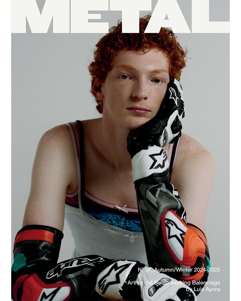 Magazine cover featuring a redhead model with freckles wearing motorcycle racing gloves, photographed indoors with a neutral background.