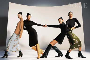 Four female models holding hands in a line against a white studio sweep backdrop wearing autumn fashion apparel