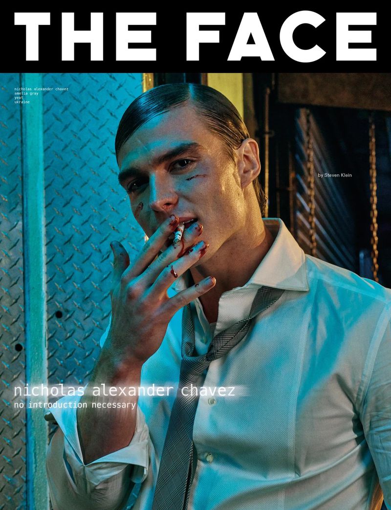 Magazine cover featuring a man with makeup and a cigarette, styled in a white shirt and tie, against a blue metal background.