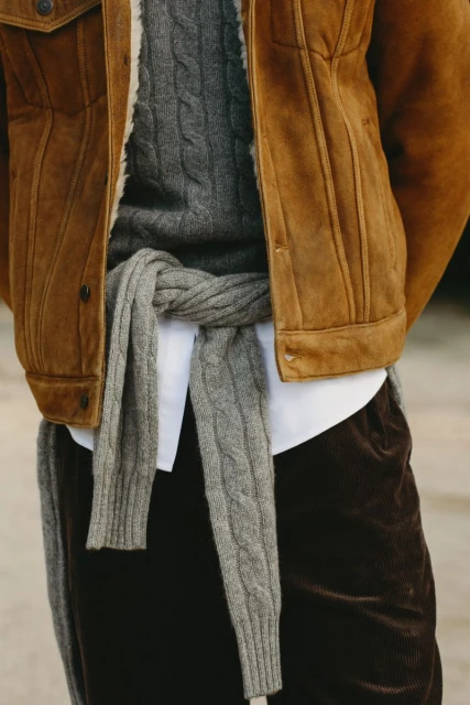Close-up of a fashionably dressed person in a brown corduroy jacket, cable knit sweater, and dark corduroy pants. Elegant menswear style.