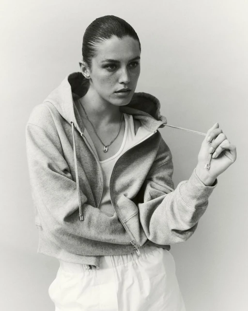 Model Emma Todt wearing an open zip-up hoodie over a tank top and holding a drawstring in a black and white portrait for Hogan.