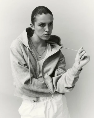 Model Emma Todt wearing an open zip-up hoodie over a tank top and holding a drawstring in a black and white portrait for Hogan.