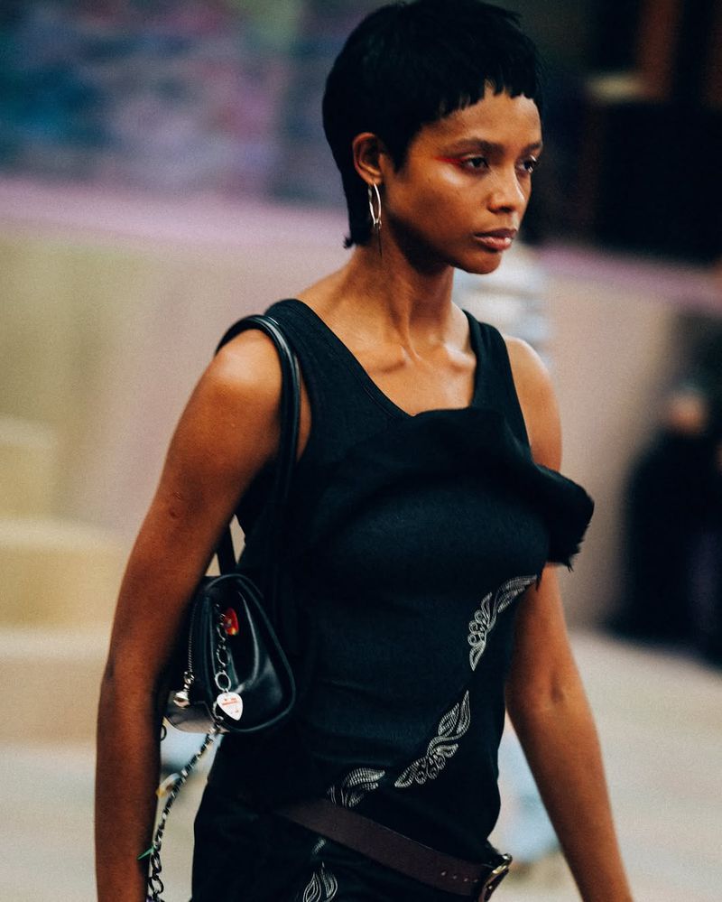 Runway fashion shot: Black woman with short hair in a black tank top and skirt with a purse on a fashion runway.