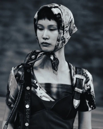 East Asian model wearing a patterned headscarf tied at the chin paired with a black corset top and western buckle strap.