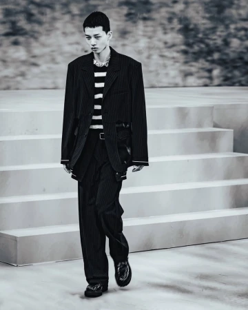Model walking down a concrete runway in a black pinstripe suit and striped sweater for ADSB ANDERSSON BELL spring/summer 2025