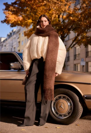 Woman standing next to a vintage bronze car wearing an off-white puffer jacket, oversized brown scarf, and wide-leg trousers.