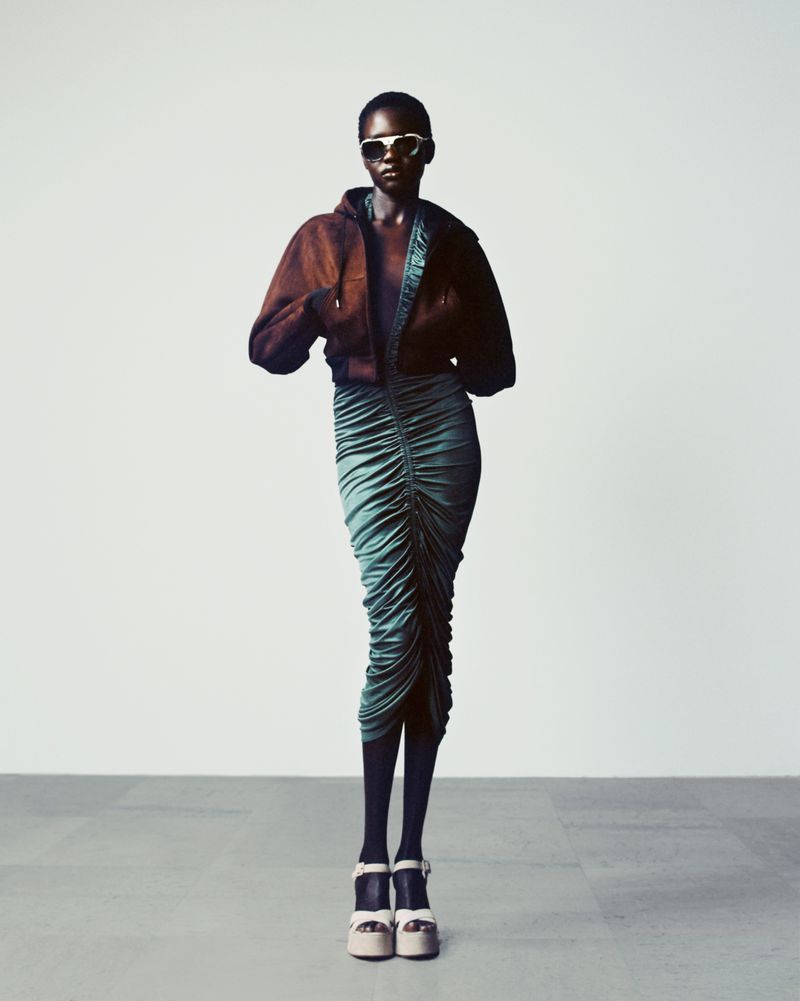Model wearing a brown cropped jacket and ruched teal midi skirt with platform sandals against a plain studio background.