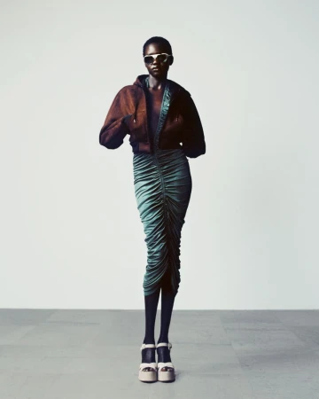 Model wearing a brown cropped jacket and ruched teal midi skirt with platform sandals against a plain studio background.