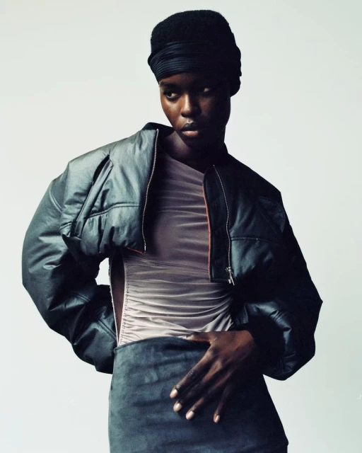Fashion portrait of an African American woman in a headwrap and leather jacket, posed in a studio with neutral background, looking at the camera.
