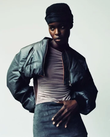 Fashion portrait of an African American woman in a headwrap and leather jacket, posed in a studio with neutral background, looking at the camera.