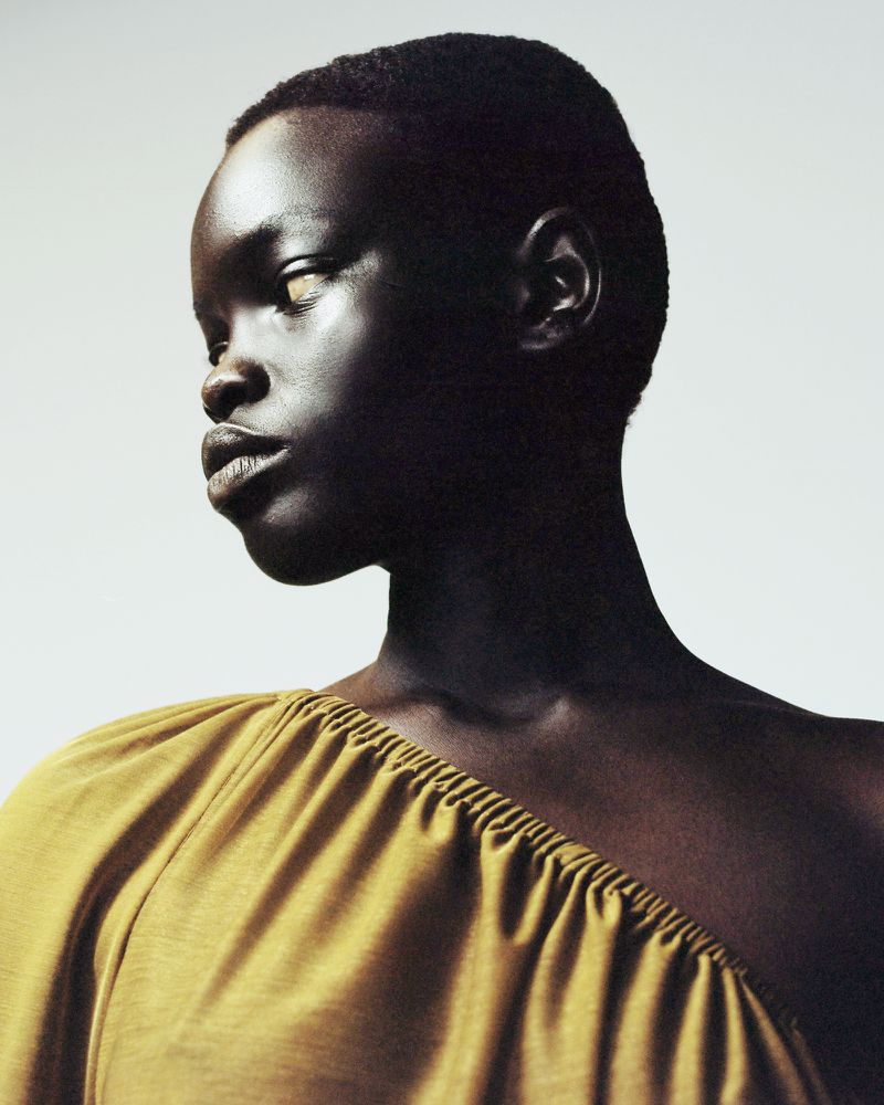 Portrait of a Black woman in yellow top looking left, shot in a photo studio with soft lighting and a minimalist background.