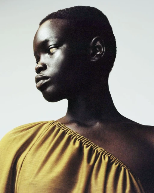 Portrait of a Black woman in yellow top looking left, shot in a photo studio with soft lighting and a minimalist background.