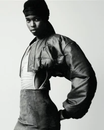 Model wearing a cropped dark bomber jacket and headwrap in a black and white backstage photograph for Atlein SS25.