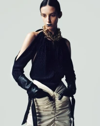 Model wearing a black halter top, white ruched skirt, and dark gloves against a plain light background