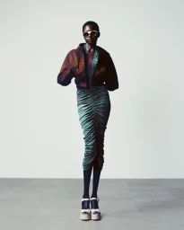 Model wearing a brown cropped jacket and ruched teal midi skirt with platform sandals against a plain studio background.