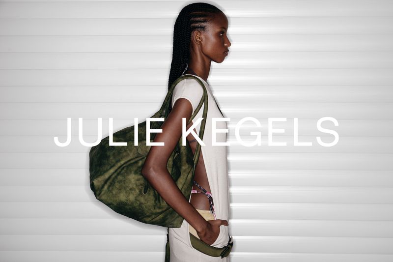 Profile of an African woman with braids carrying an olive duffel bag, standing against a white corrugated wall, with brand text.