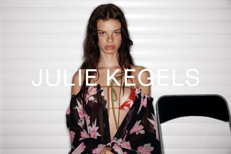 Portrait of a young adult woman with long brown hair wearing a floral cover-up in a studio with a chair in the background.