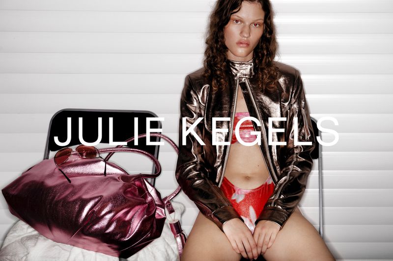 Young adult woman poses in metallic jacket, floral bikini, with purse and sunglasses in a studio setting. Fashion editorial.
