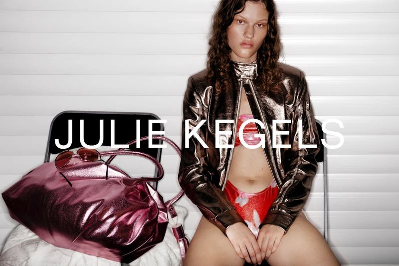 Young adult woman poses in metallic jacket, floral bikini, with purse and sunglasses in a studio setting. Fashion editorial.