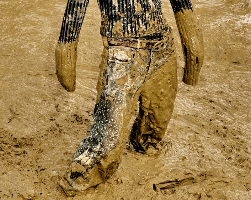 Person waist-down stands in thick, deep, brown mud. Mud covers clothing, suggesting immersion or play in a muddy environment.