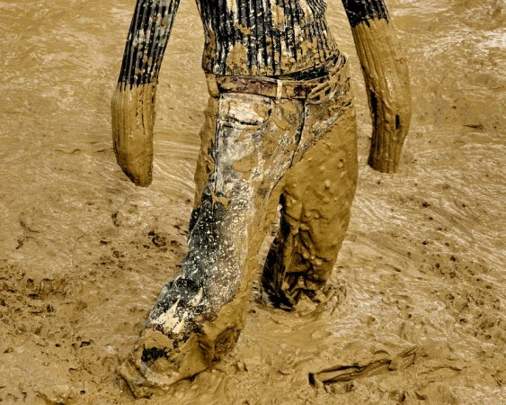 Person waist-down stands in thick, deep, brown mud. Mud covers clothing, suggesting immersion or play in a muddy environment.