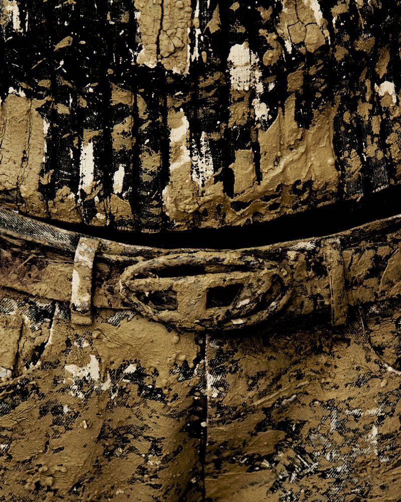 Abstract fashion close-up featuring clothing covered in brown mud, showcasing texture and an artistic design aesthetic.