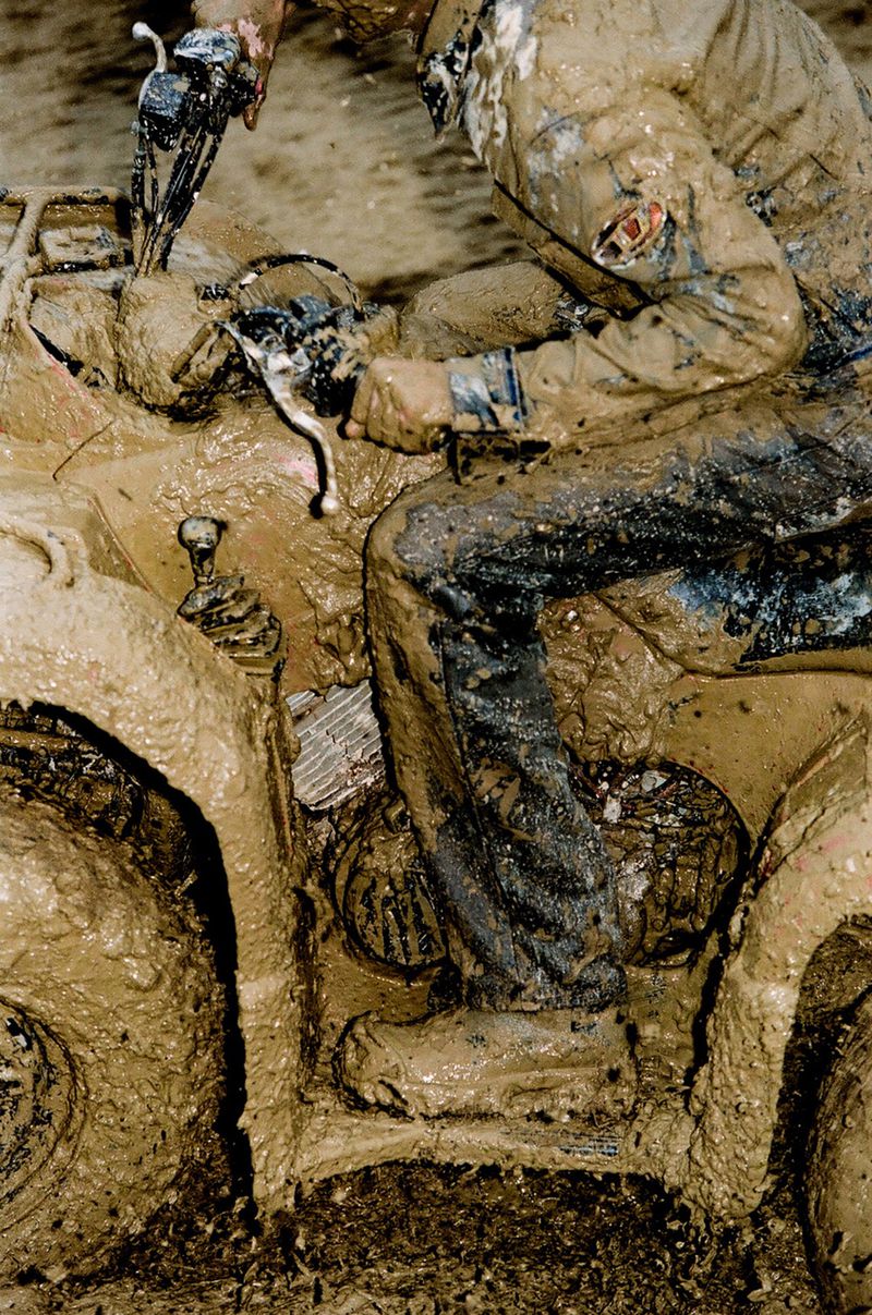 Person riding a mud-covered ATV, with a focus on the extreme mud and vehicle details, showcasing an off-road motorsport activity.