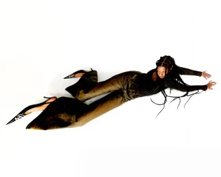 Model lying horizontally on a white seamless background wearing dark trousers and pointed high heels