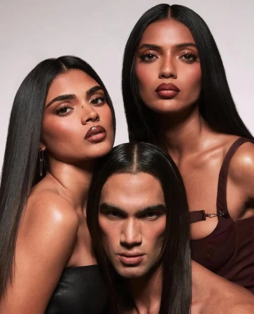 Three models pose in a studio. Two women and one man with straight dark hair. The women wear brown lipstick and strapless tops.
