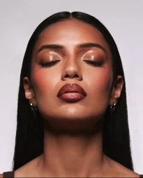 Close-up portrait of a woman with glossy makeup and closed eyes against a neutral backdrop for Patrick Ta.