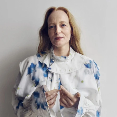 Portrait of a fair-skinned adult female with long red hair in a white collared shirt with blue dye patterns against a white background.