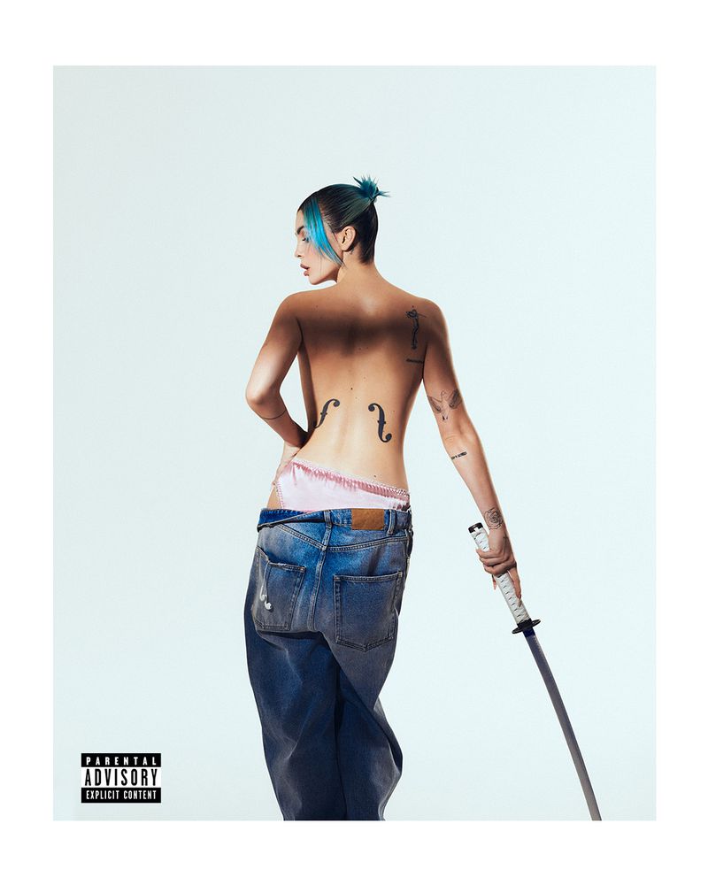 Topless woman with blue hair, back tattoos, and jeans poses in studio with katana, creating a striking and edgy visual statement.