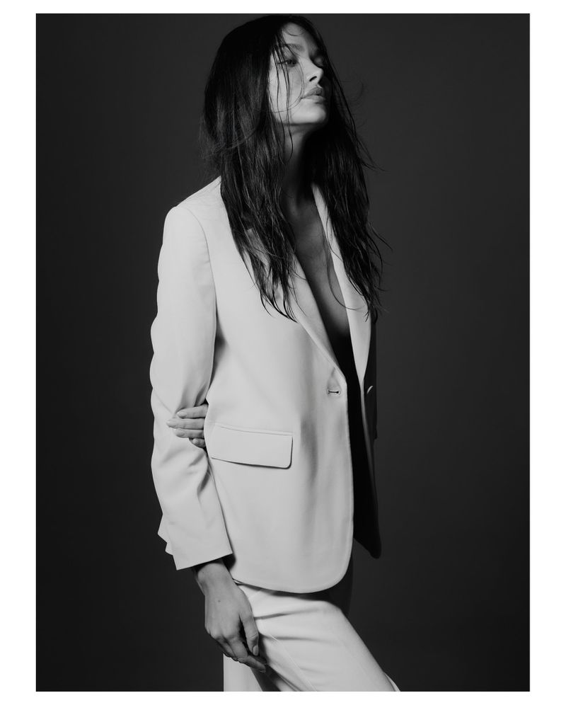 Black and white portrait of Denisa Ciocoiu wearing an open light suit jacket against a dark studio backdrop.