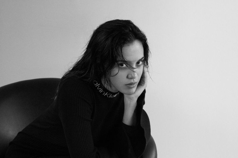 Portrait of a young woman in a black turtleneck sweater sitting in a chair against a white background in a black and white studio photograph.