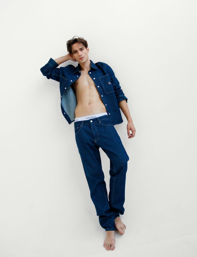 Male model wearing open denim shirt and jeans against a plain white background for Calvin Klein.