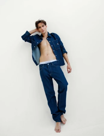 Male model wearing open denim shirt and jeans against a plain white background for Calvin Klein.