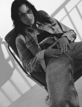 Model Iasonas Laios seated in a chair wearing a denim jacket and jeans in black and white for Calvin Klein F/W 23.